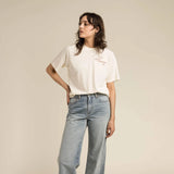 Woman wearing a white t-shirt and light blue jeans against a beige background